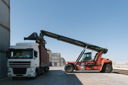 Crane Lifting Cargo Container On Truck On Industrial Site