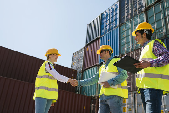 Workers shaking hands in front of cargo containers on industrial site