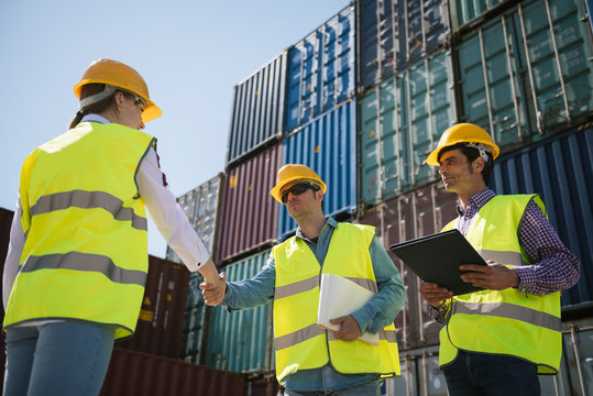 Workers shaking hands in front of cargo containers on industrial site