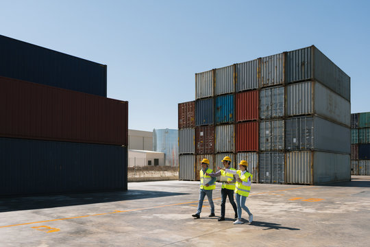 Workers walking together near stack of cargo containers on industrial site