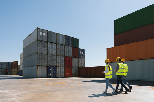 Workers walking together near stack of cargo containers on industrial site