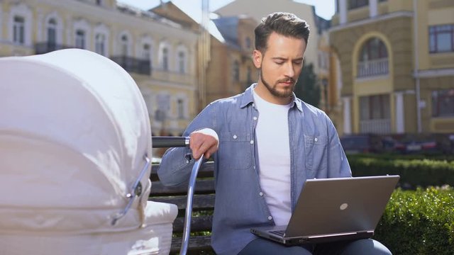 Modern young dad working laptop and swinging baby pram, multitasking lifestyle