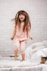 Naklejka premium cute little child girl fooling around in bed. child jumping on bed