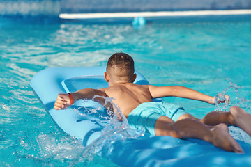  Caucasian boy  is  laying on blue  inflatable mattress at hotel swimming pool. He is enjoying his summer vacations.