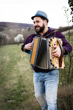 Portrait of bearded man playing accordion on a meadow