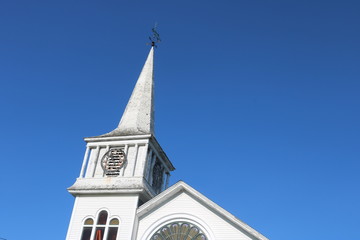Old weathered wooden white New England church with steeple and clock