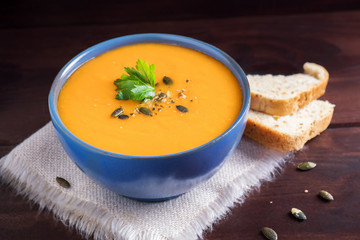 Pumpkin soup in a bowl served with parsley, olive oil and pumpkin seeds. Vegan soup. Dark wooden background.