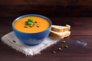 Pumpkin soup in a bowl served with parsley, olive oil and pumpkin seeds. Vegan soup. Dark wooden background.
