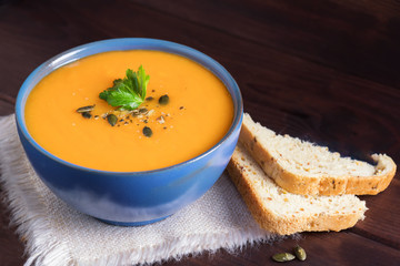 Pumpkin soup in a bowl served with parsley, olive oil and pumpkin seeds. Vegan soup. Dark wooden background.
