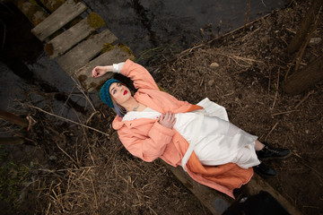Stylish young girl resting on the river shore, lying on a small wooden bridge