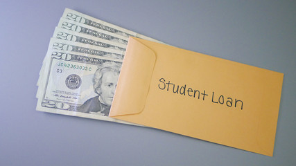 A yellow envelope on a gray table, containing cash for student loans.