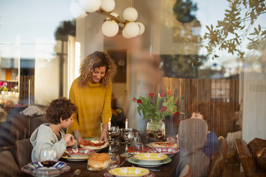 Mother serving pizza to boys on dining table at home seen through window