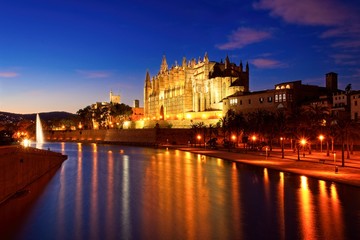 Palma cathedral illuminated at dusk with lake, fountain and reflections on water, mallorca, spain.