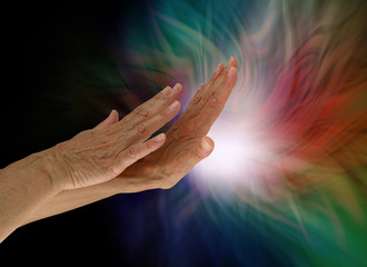 Sending light and healing energy out where it is needed - female hands appearing to push out white light from the palm with darkness on left and multiple colours around the light source