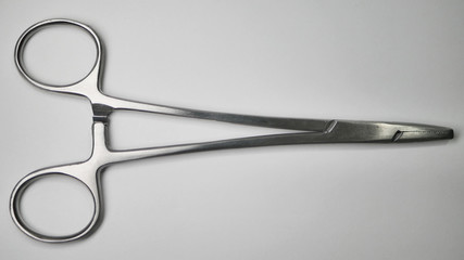 A pair of small stainless steel surgical medical grade needle holder clamps laying closed on a white table.