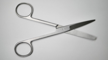 A pair of large stainless steel surgical medical grade scissors laying open on a white table.
