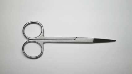 A pair of small stainless steel surgical medical grade scissors laying closed on a white table.