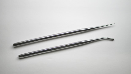 A pair of stainless steel surgical pointed and blunt medical grade probes on a white table.