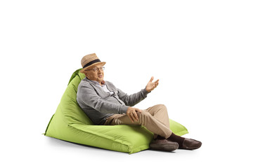 Senior man with face expression resting on a bean-bag armchair and gesturing with hand