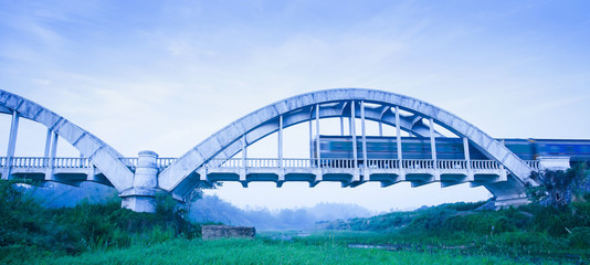 Old train passing the Tha Chomphu Bridge in blue misty morning, the ancient railway bridge of Thailand.