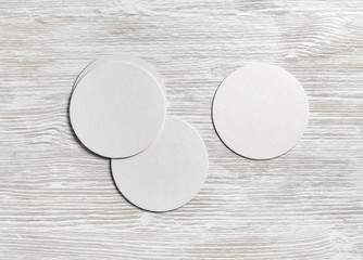 Blank white beer coasters on light wood table background. Flat lay.