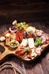 Cutting board with prosciutto, salami, cheese,bread and olives on dark wooden background