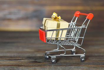 Christmas gift shopping concept. Shopping cart and gift box on wooden background with copy space
