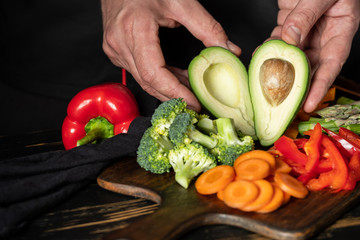 Chef cooking assorted raw vegetables - avocado, carrot, paper, asparagus, broccoli and greens on wooden table background.