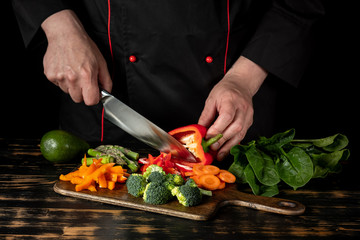 Chef cooking assorted raw vegetables - carrot, paper, asparagus, broccoli and greens on wooden table background.