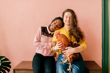 Young stylish female interracial couple with chikcne in their hands hugging in home interior.