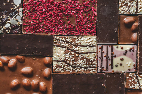 Background with milk, dark and white chocolate bar pieces. Chocolate pazl with hazelnut, peanut, dried raspberries and raisins