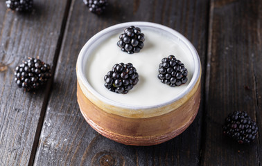 Serving white yogurt in ceramic bowl with blueberries and honey on top on rustic wooden desk.
