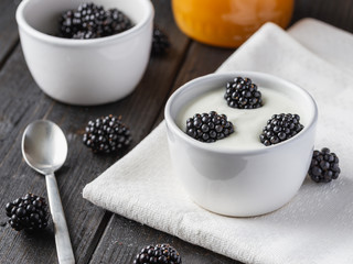 Fototapeta na wymiar Serving white yogurt in ceramic bowl with blueberries and honey on top on black wooden desk.