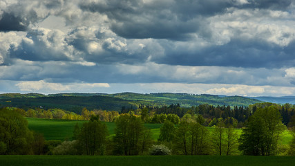Fototapeta premium A summer hilly landscape with dark, heavy clouds flowing in the sky.