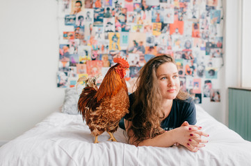 Long haired brunette  lying on bed with chicken on 90s style wall on background