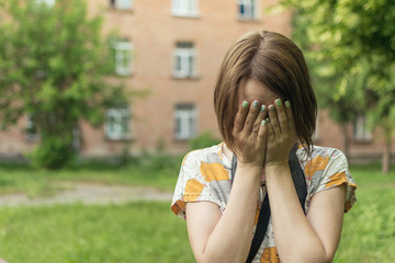 A depressed woman covered her face with her hands against the background of an old house.