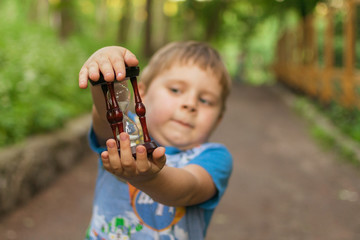 A little boy holds an hourglass in nature.