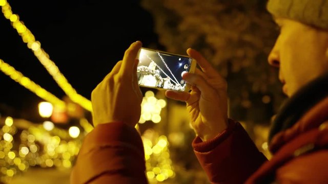 Young man in red jacket makes photos with smartphone in the evening on Christmas illumination background. Shot on Red camera