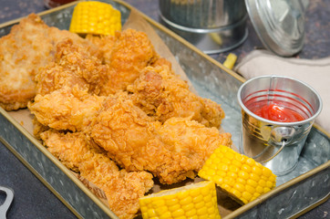 Dinner table with fried chicken, wings and strips, french fries, sweet corn and red sauce. Homemade southern fried chicken meal