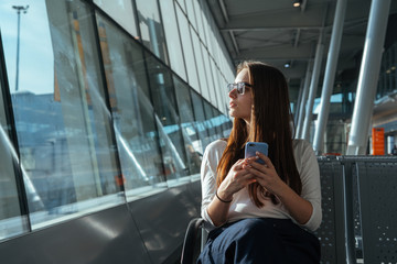 Passenger woman in casual clothes sitting at the gate and using smartphone while waiting for a...