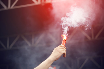 The man at the energetic rock concert lit and raised in his hand up a red Smoking signal fire