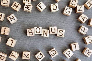 the word bonus wooden cubes with burnt letters, cash bonuses at work, gray background top view, scattered cubes around random letters