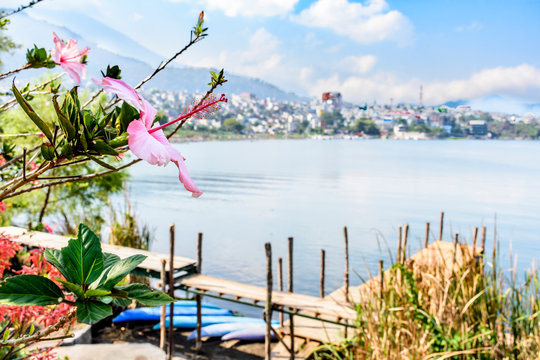 Hibiscus flowers in foreground with jetty, canoes & Lake Atitlan behind & town of Santiago Atitlan, Guatemala in background.