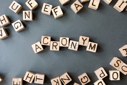 the word acronym wooden cubes with burnt letters, use of acronyms in the modern world, gray background top view, scattered cubes around random letters