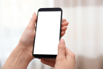 Woman holding smartphone with blank screen on blurred background, closeup of hands. Space for text