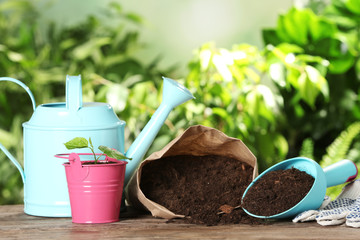 Composition with bag of soil and gardening equipment on wooden table against blurred background,...