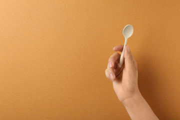 Woman holding empty small spoon on color background, closeup. Space for text