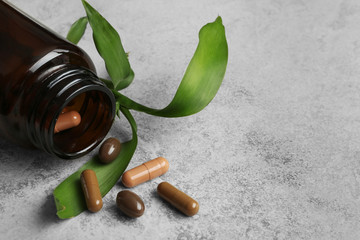 Bottle with vitamin capsules and green leaves on table, space for text