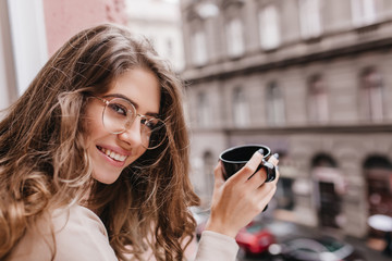 Close-up portrait of wonderful woman holding cup of latte on blur city background and looking to...