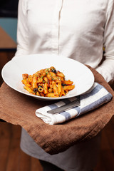 Waitress is holding a dish with vegan penne in tomato sauce